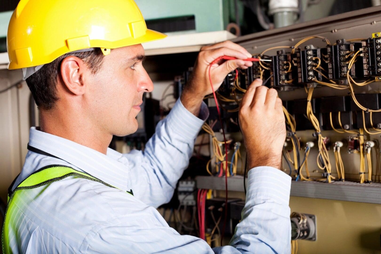 A man in yellow hard hat working on wires.