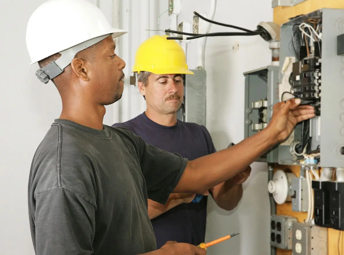 Two men in hard hats working on electrical equipment.