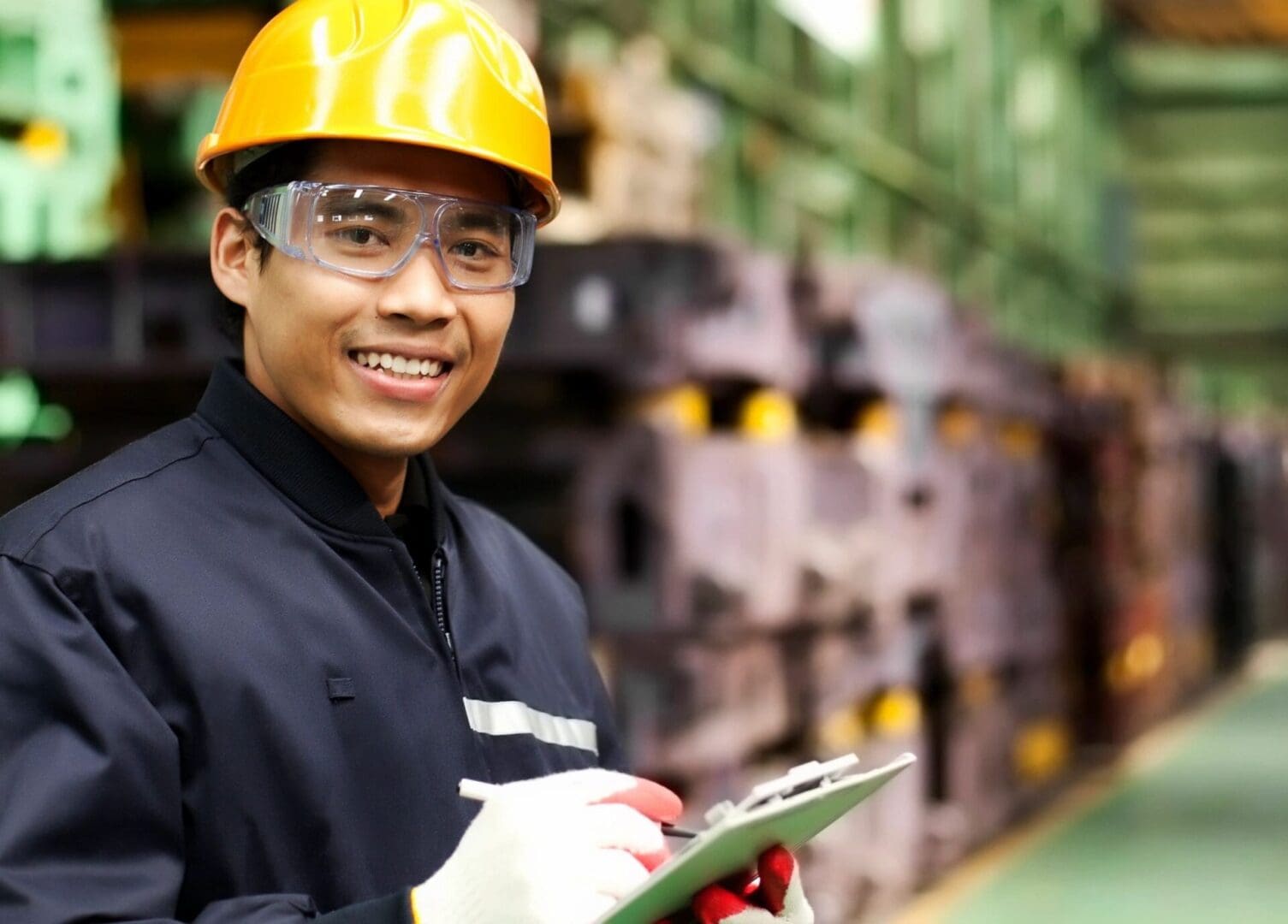 A man in an industrial setting holding a clipboard.